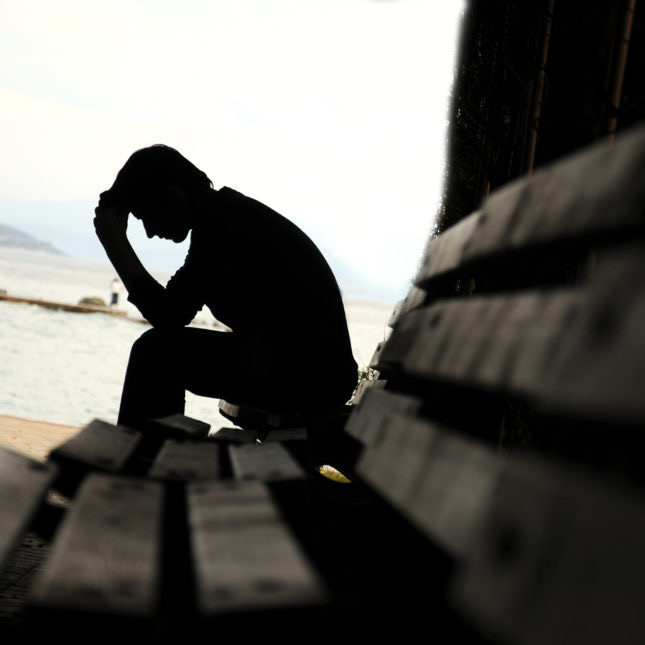 depressed young man sitting on the bench Young man sitting looking upset